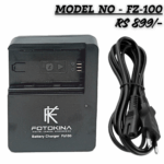 "FOTOKINA FZ-100 Digital Camera Battery Charger, black, shown with a two-pin AC power cord. The charger features an LED indicator and is clearly marked with the model number 'FZ100'."